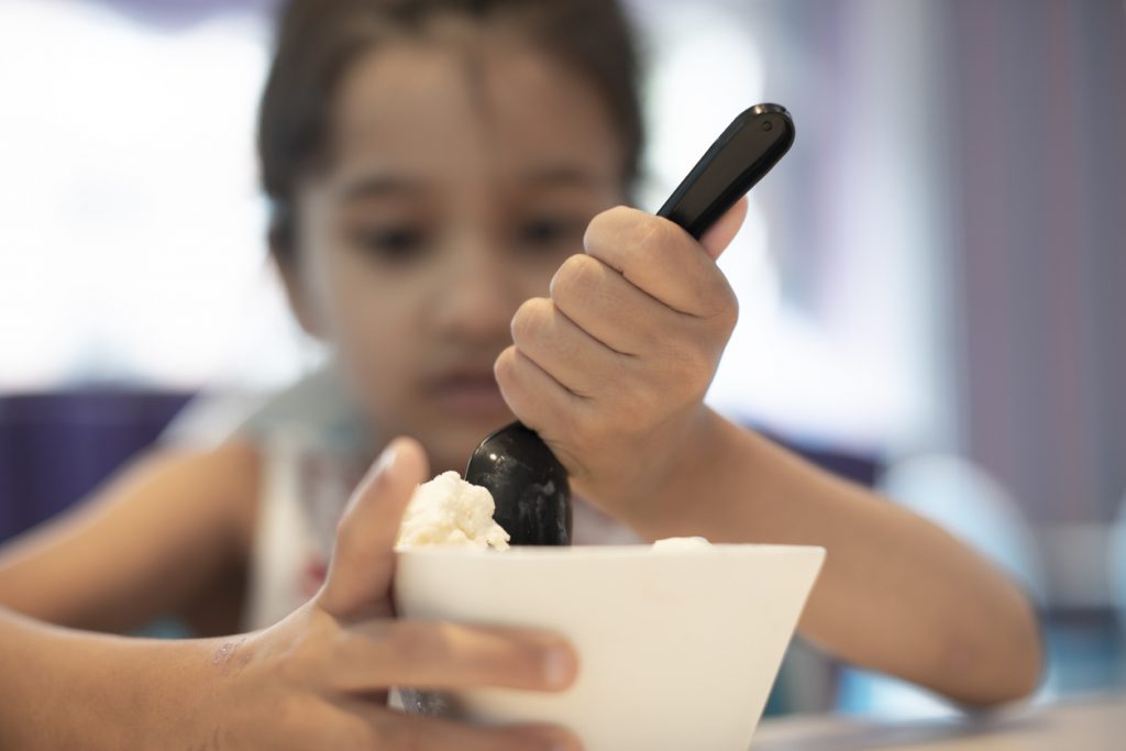 Little girl bending spoon trying to eat hard ice cream