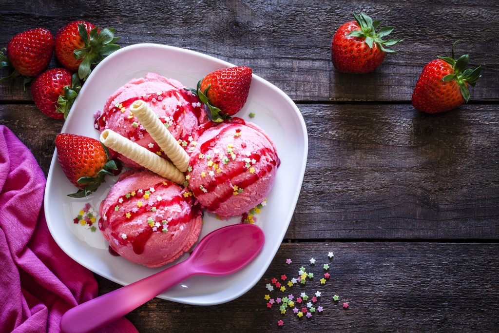 Three scoops of soft strawberry ice cream with wafers and fresh strawberries on a plate