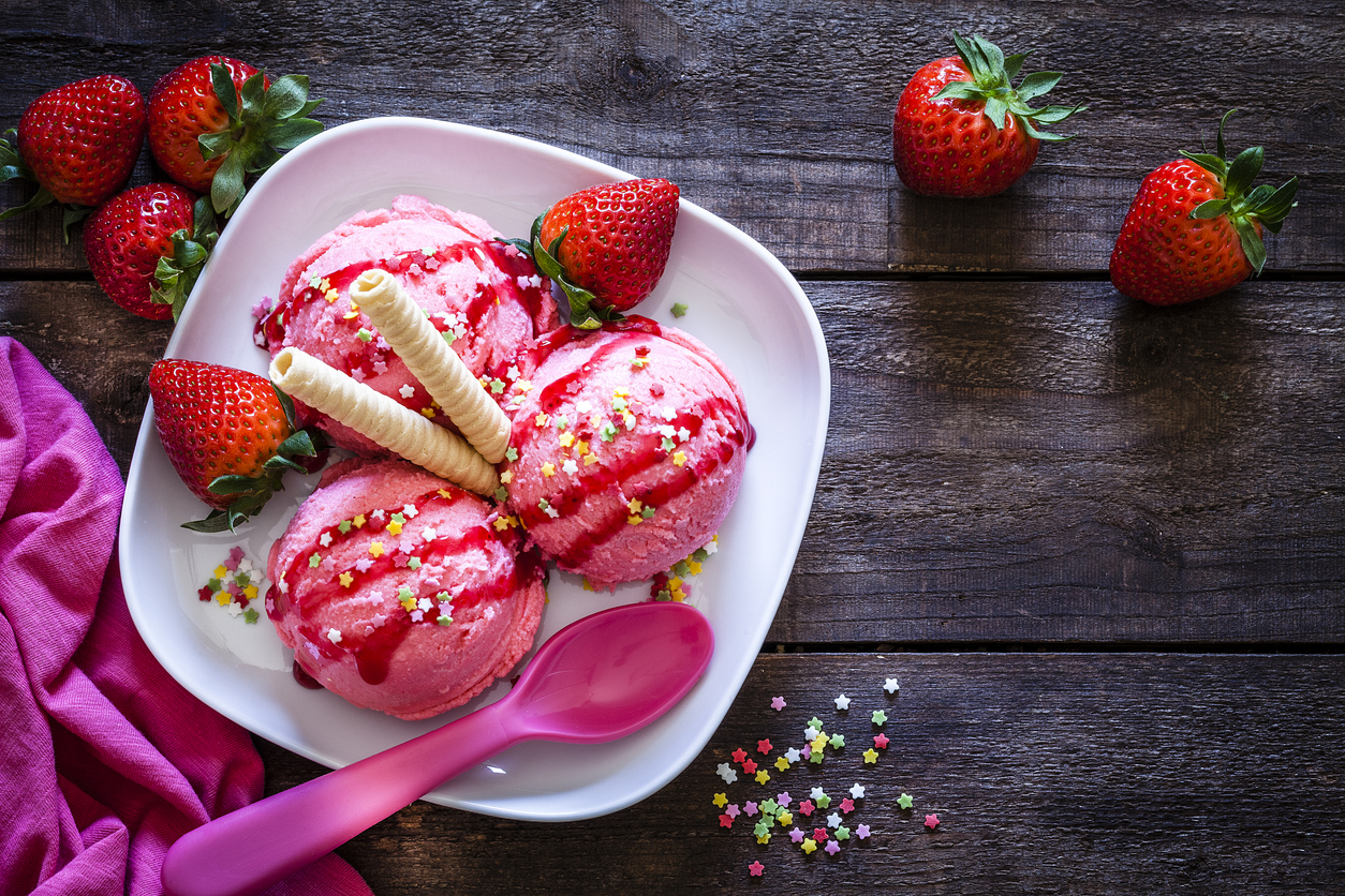 Three scoops of soft strawberry ice cream with wafers and fresh strawberries on a plate
